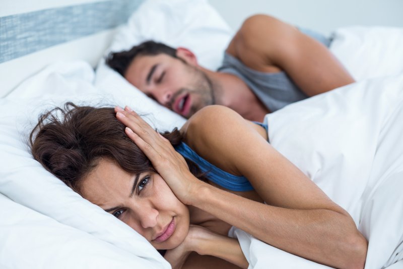 a woman covering her ears while her husband snores